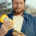 Homem colocando mostarda Heinz em cachorro-quente