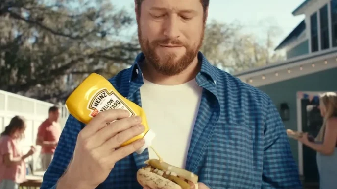 Homem colocando mostarda Heinz em cachorro-quente