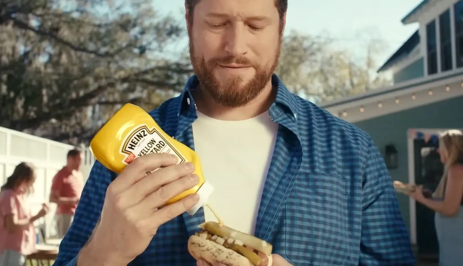 Homem colocando mostarda Heinz em cachorro-quente