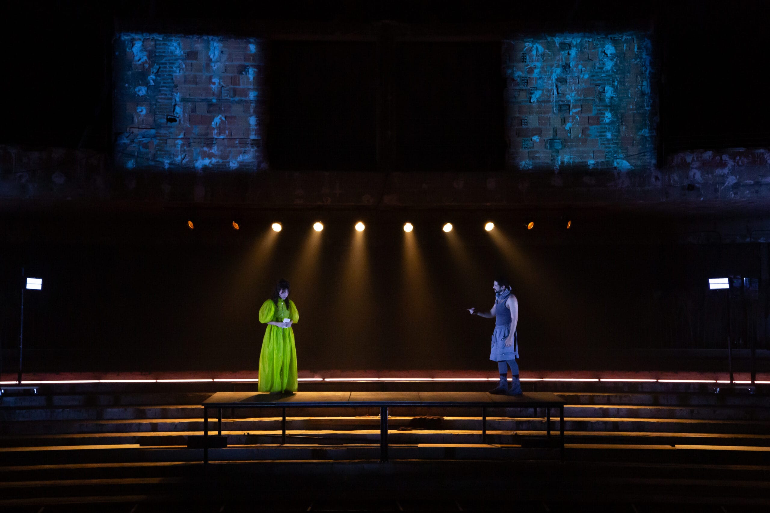Dois atores em palco iluminado por refletores