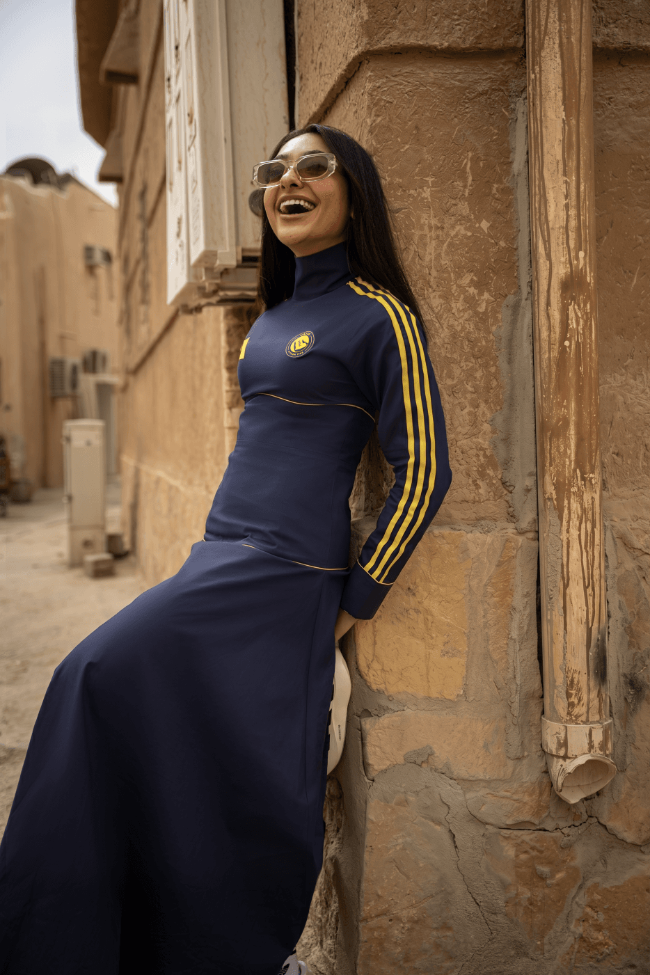 Mulher de vestido azul encostada em parede rústica