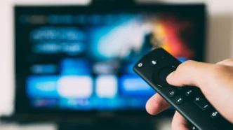 Pessoa segura controle remoto diante de televisão ligada, representando o consumo de documentários esportivos em streaming.