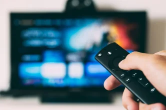 Pessoa segura controle remoto diante de televisão ligada, representando o consumo de documentários esportivos em streaming.