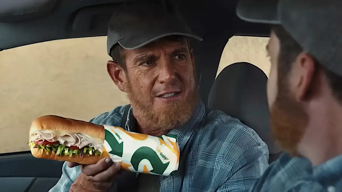 Will Arnett, caracterizado como o subconsciente, oferece um sanduíche da Subway a um homem dentro de um carro